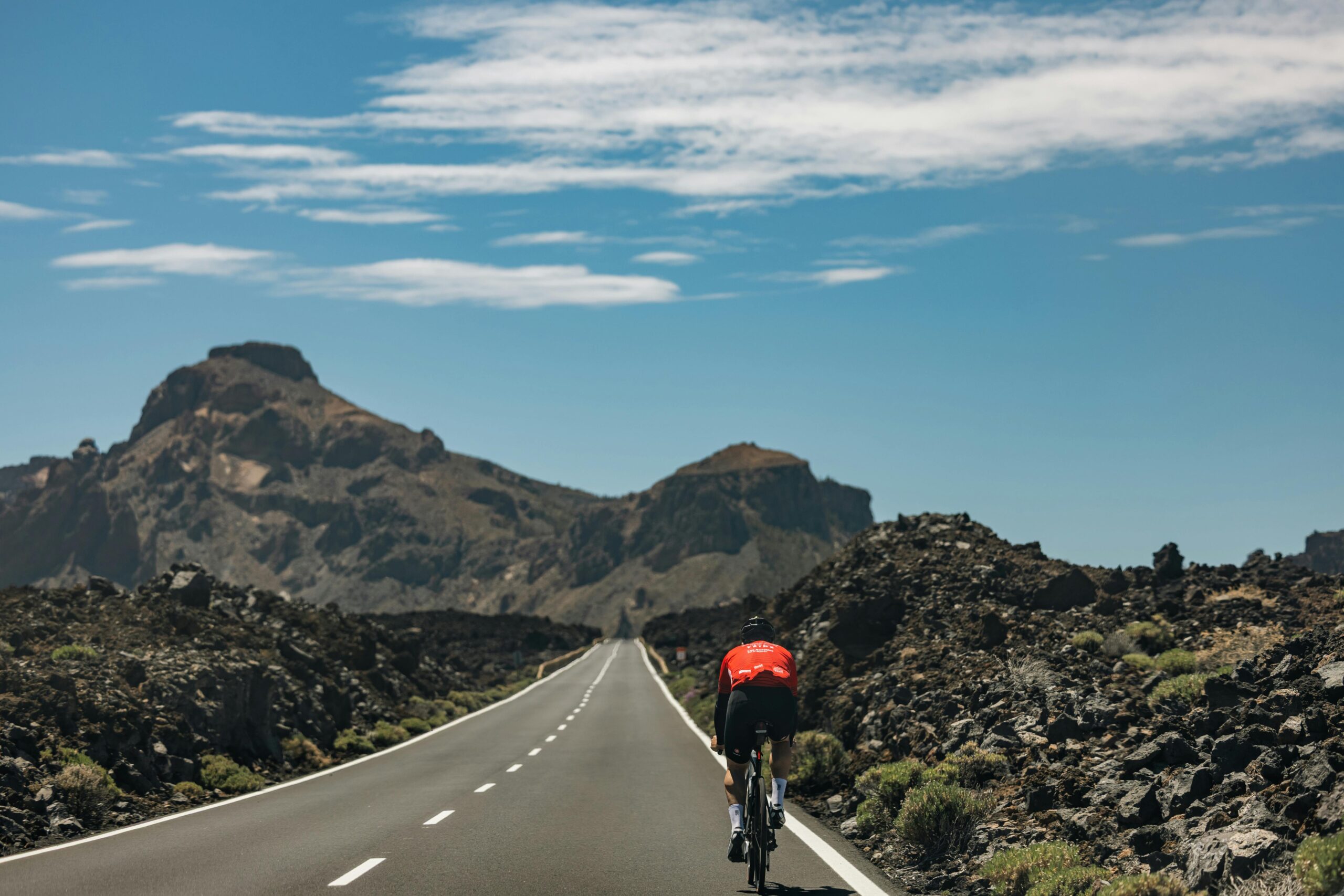 Cyclist on an open road with stunning volcanic mountains under a clear sky.